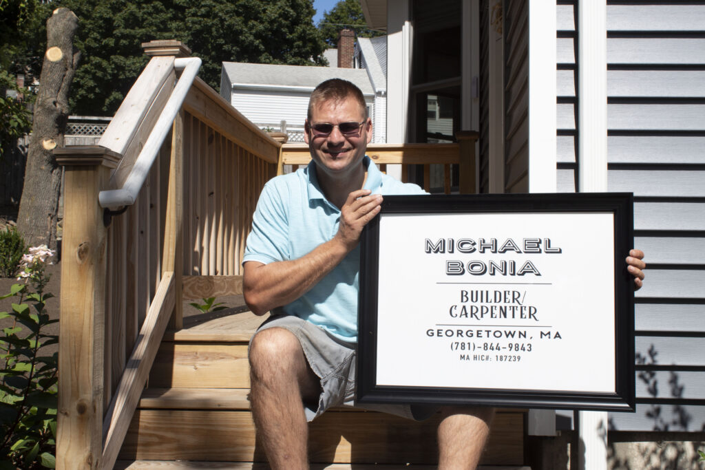 Mike bonia builder sitting with sign outside of a completed project
